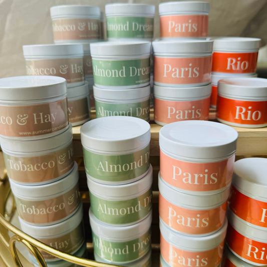 Small travel tin candles in different scents with colourful labels. Paris, Almond Milk, Tobcaco & Hay and Rio.