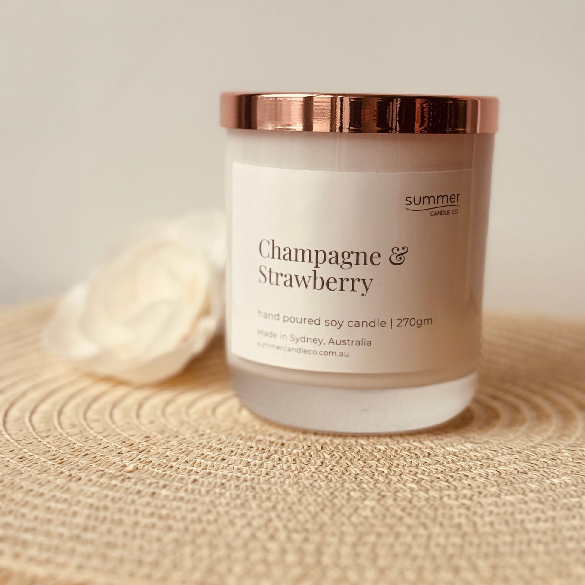 Hand-poured soy wax candle in a white jar with a rose gold lid, scented with Champagne & Strawberry. A sparkling, fruity blend with notes of ripe strawberries and bubbly champagne. Clean-burning and perfect for gifting or adding a festive touch.