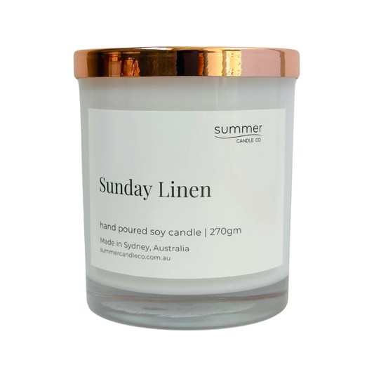 Clear glass soy wax candle jar labeled “Sunday Linen” with a sleek rose gold lid, featuring minimalist and elegant packaging. The candle evokes fresh, clean linen scents, perfect for creating a calm and cozy atmosphere at home. Ideal as a stylish gift or for enhancing your living space with subtle, soothing fragrance and modern home decor appeal.