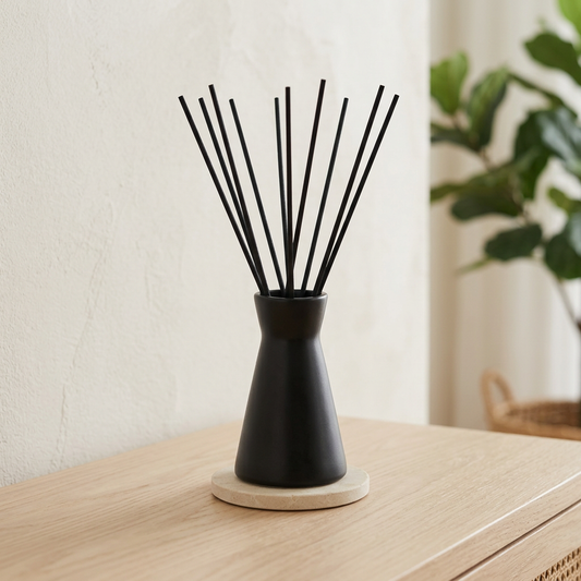 Black ceramic reed diffuser on a pale timber console with subtle greenery