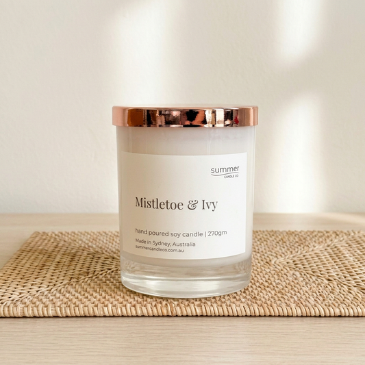 Mistletoe & Ivy soy wax candle with rose-gold lid on a natural rattan placemat