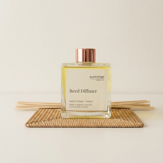 Clear cubic reed diffuser with rose-gold cap on a rattan mat