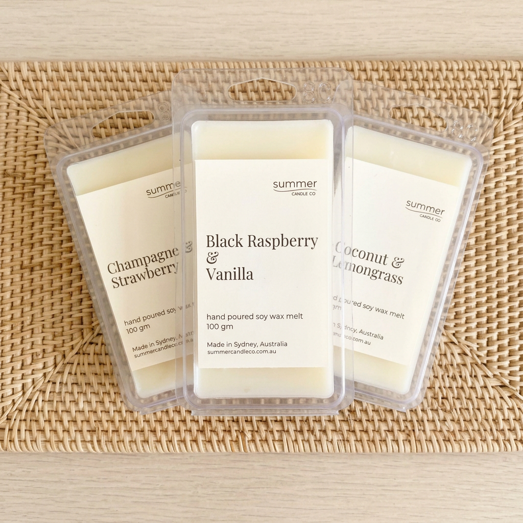 Three Summer Candle Co soy wax melt clamshells lying flat on a natural rattan placemat: Champagne & Strawberry, Black Raspberry & Vanilla, Coconut & Lemongrass